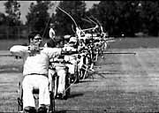 A line of archers in wheelchairs draw aim on their targets.