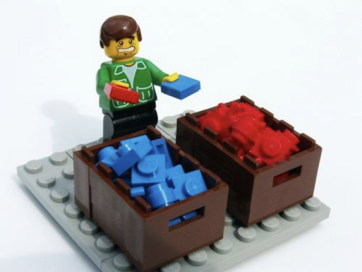 A lego man sorting red and blue lego pieces into boxes.